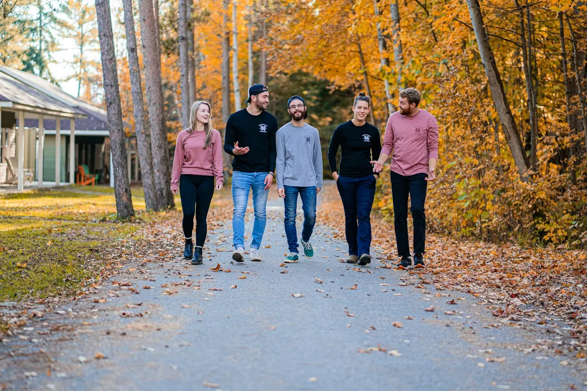 Five adults walking along a path lined with autumn trees and fallen leaves