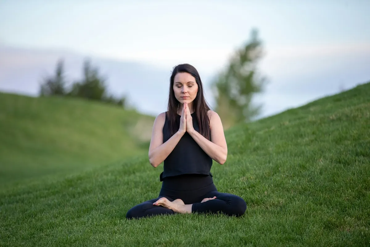 woman in black tank top and black pants sitting on green grass field during dayt