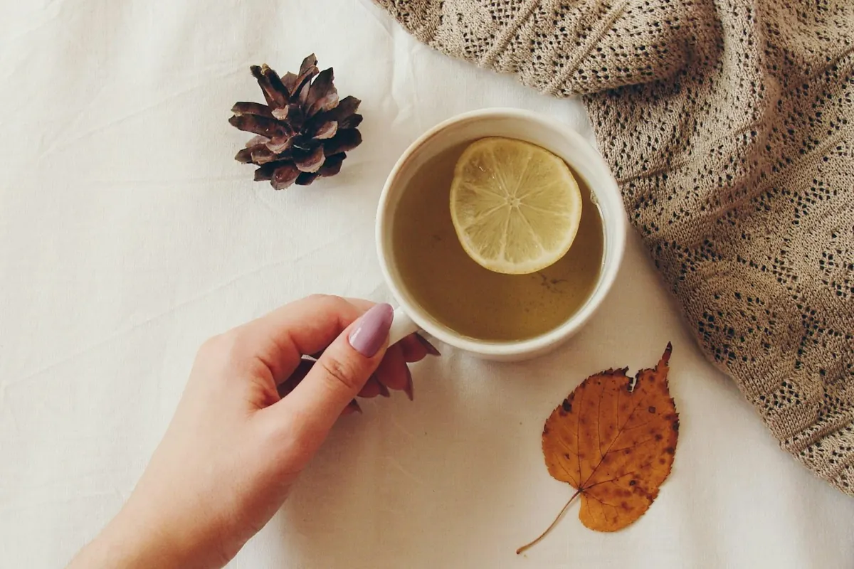 Hand holding cup of tea with lemon slice and pinecone