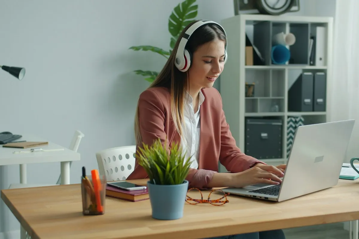 Young woman wearing headphones works on laptop at desk